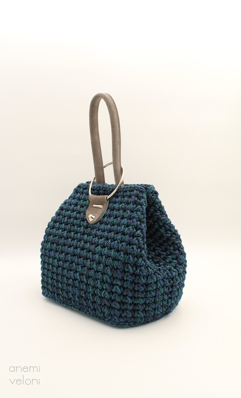 May include: A dark blue and green crocheted handbag with a gray leather handle and a silver ring.