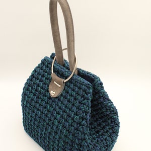 May include: A blue and green crocheted handbag with a brown leather handle and a silver ring.