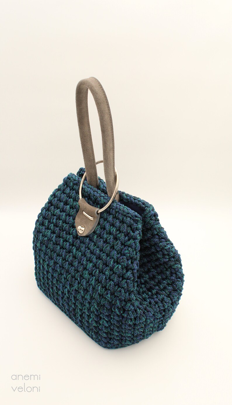May include: A blue and green crocheted handbag with a brown leather handle and a silver ring.