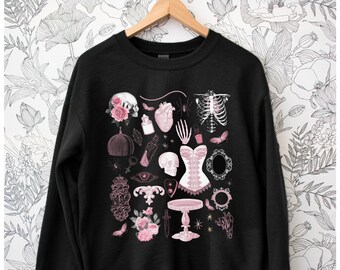May include: Black sweatshirt with a pink and white graphic print of various gothic and occult symbols, including a skull, a heart, a spider, a skeleton, a corset, a dagger, a flower, and a mirror.