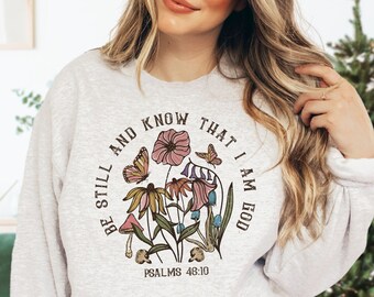 May include: A gray sweatshirt with a floral design and the text "Be still and know that I am God" with the scripture reference "Psalms 46:10".
