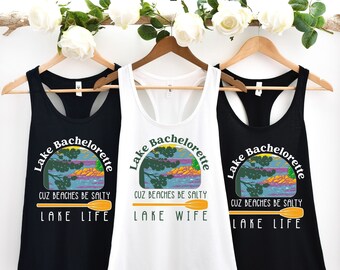 May include: Three tank tops with a lake scene and the text "Lake Bachelorette" with a paddle and the text "Cuz beaches be salty" and either "Lake Life", "Lake Wife" or "Lake Life".