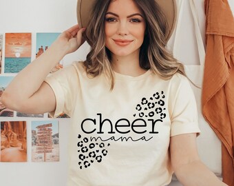 May include: A cream colored t-shirt with a black leopard print design and the text "cheer mama" in black.