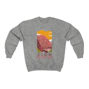 May include: A gray sweatshirt with a graphic of a mountain range in Zion National Park. The graphic is in a vintage style with a yellow, orange, red, and green color scheme. The text "Zion National Park" is printed below the graphic.