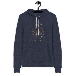 May include: A navy blue hoodie with a gold Pisces zodiac sign and constellation design. The text "PISCES" is printed below the design.