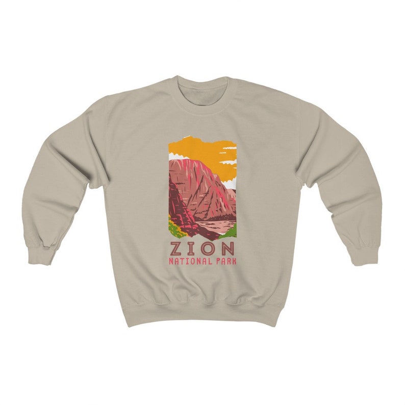 May include: A beige sweatshirt with a graphic of a mountain range in Zion National Park. The graphic is in shades of red, orange, yellow, and green. The text "Zion National Park" is printed below the graphic.