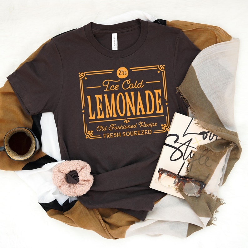 May include: A brown t-shirt with a vintage-style graphic that reads "25&cent; Ice Cold Lemonade Old Fashioned Recipe Fresh Squeezed".