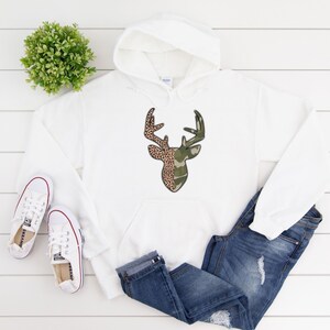 May include: White hooded sweatshirt with a deer head graphic. The deer head is split in half, with one side featuring a camouflage pattern and the other side featuring a leopard print.