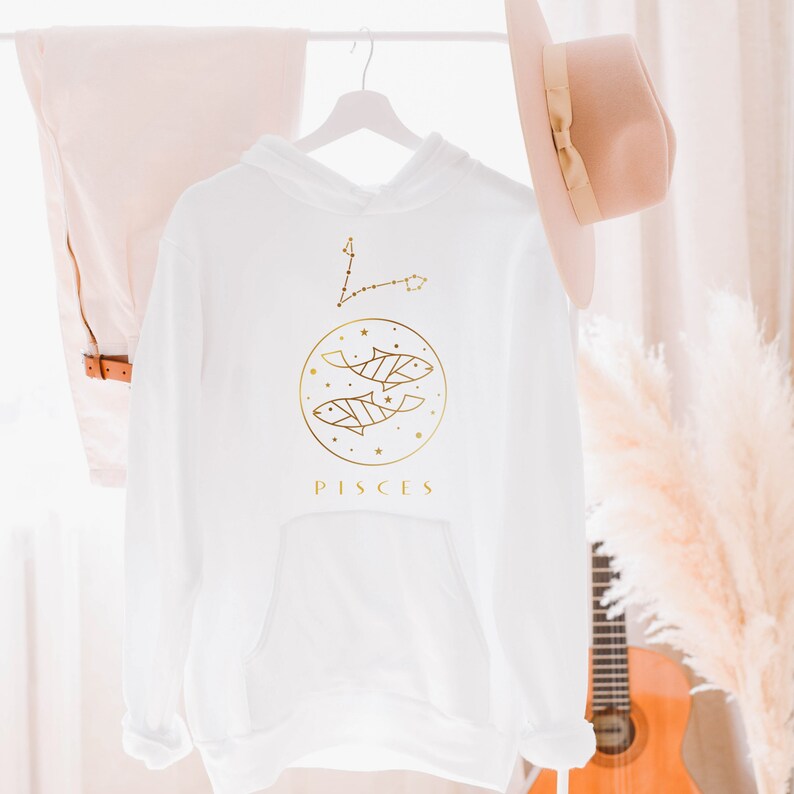 May include: White hoodie with a gold Pisces zodiac sign and constellation graphic. The sign features two fish and the word "PISCES" in gold lettering.