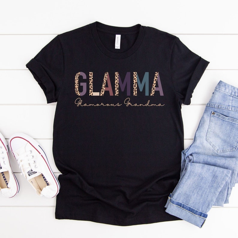 May include: Black t-shirt with the text "GLAMMA Glamorous Grandma" in colorful letters with a leopard print pattern.