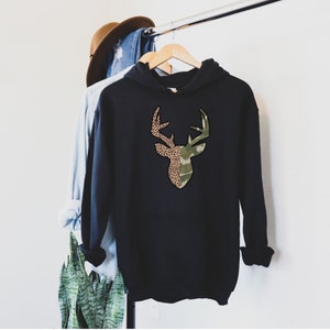 May include: Black hooded sweatshirt with a deer silhouette design. The deer's antlers are outlined in brown and the head is split in half with one side featuring a camouflage pattern and the other side featuring a leopard print.