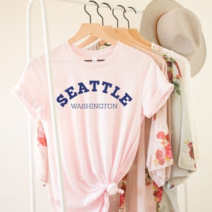 May include: A pink t-shirt with the text "SEATTLE WASHINGTON" in navy blue lettering.