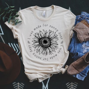 May include: A beige t-shirt with a black sunflower graphic and the text "I was made for sunny days".