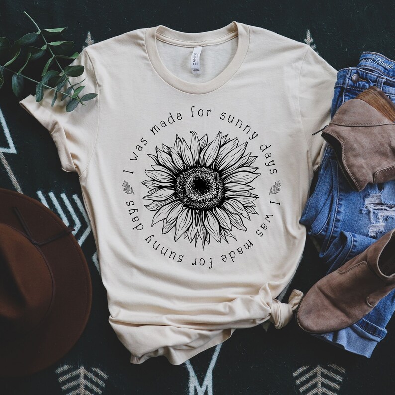 May include: A beige t-shirt with a black sunflower graphic and the text "I was made for sunny days".