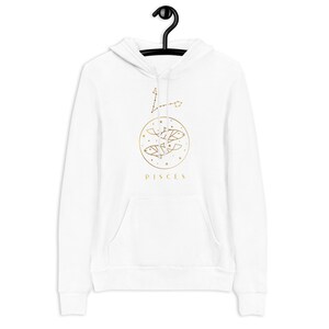 May include: White hoodie with a gold Pisces zodiac sign and constellation design. The design features two fish and stars in a circle with the word "Pisces" below.