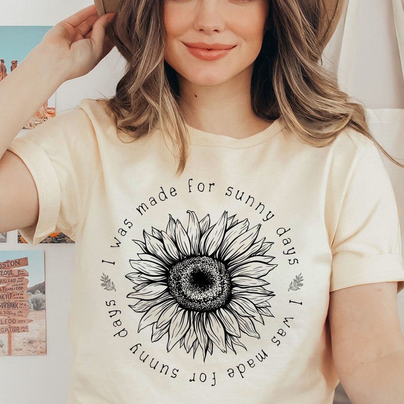 May include: A cream colored t-shirt with a black and white sunflower graphic and the text "I was made for sunny days I was made for sunny days".