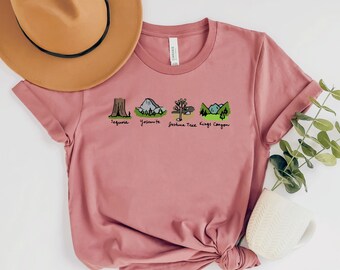 Könnte beinhalten: Ein pinkfarbenes T-Shirt mit einer Grafik von fünf Nationalparks: Sequoia, Yosemite, Joshua Tree, Kings Canyon und einem Baum. Der Text "Sequoia", "Yosemite", "Joshua Tree" und "Kings Canyon" steht unterhalb jeder Parkgrafik.