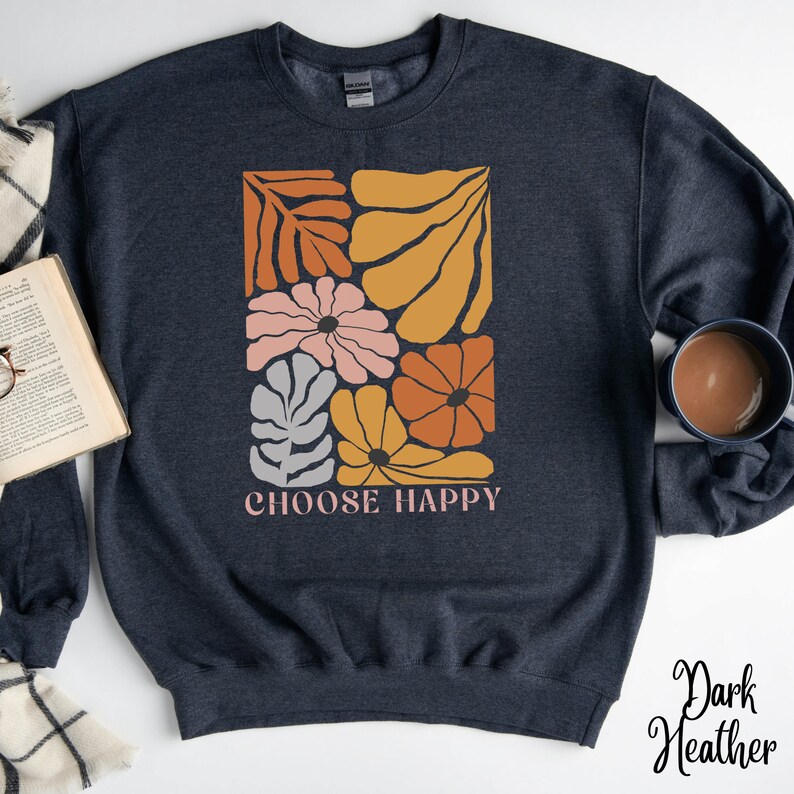 May include: Dark heather grey sweatshirt with a graphic design of stylized flowers and leaves in shades of orange, yellow, pink, and grey. The text "CHOOSE HAPPY" is printed below the graphic.