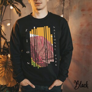 Könnte beinhalten: Schwarzes Sweatshirt mit einem Grafikdruck einer Berglandschaft und dem Text "Zion National Park".