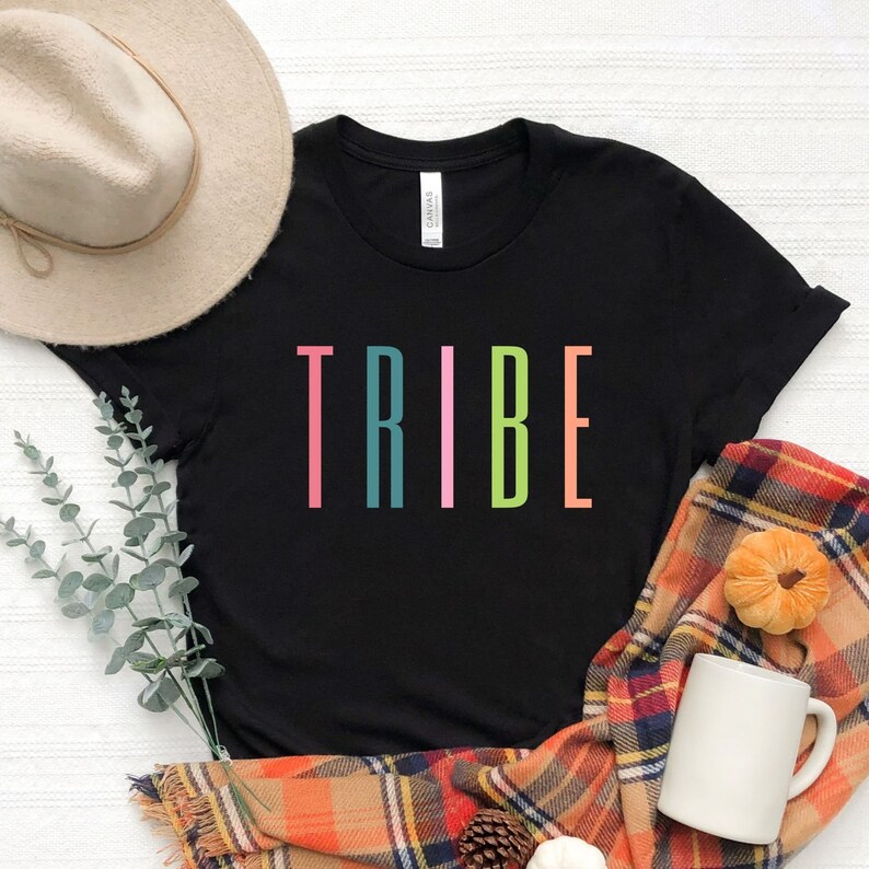 以下が含まれることがあります： カラフルな縦文字で「TRIBE」とプリントされた黒いTシャツ