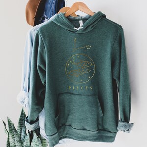 May include: A dark green hoodie with a gold graphic of the Pisces zodiac sign and the word "Pisces" printed below.