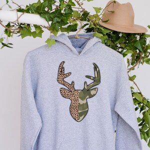 May include: A gray hooded sweatshirt with a deer head design. The deer's antlers are half camouflage and half leopard print.