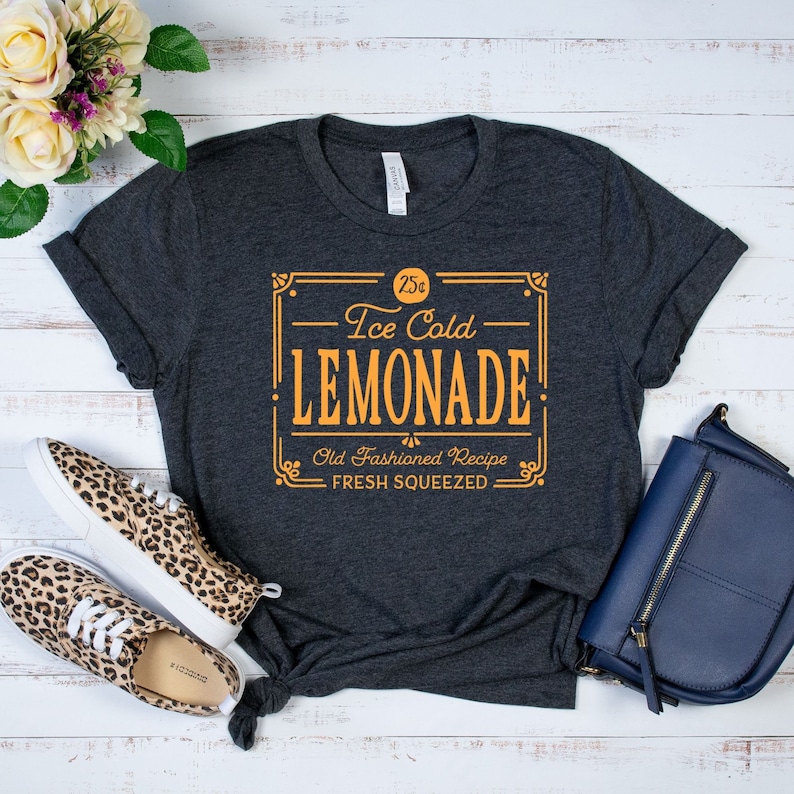 May include: A dark gray t-shirt with a vintage-style graphic design that reads "25&cent; Ice Cold Lemonade Old Fashioned Recipe Fresh Squeezed".