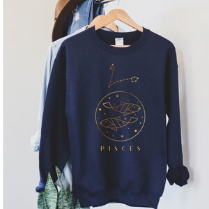 May include: Navy blue sweatshirt with a gold outline of the Pisces constellation and two fish. The text "PISCES" is printed below the design.