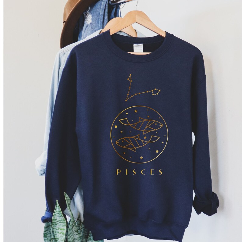 May include: Navy blue sweatshirt with a gold outline of the Pisces constellation and two fish. The text "PISCES" is printed below the design.