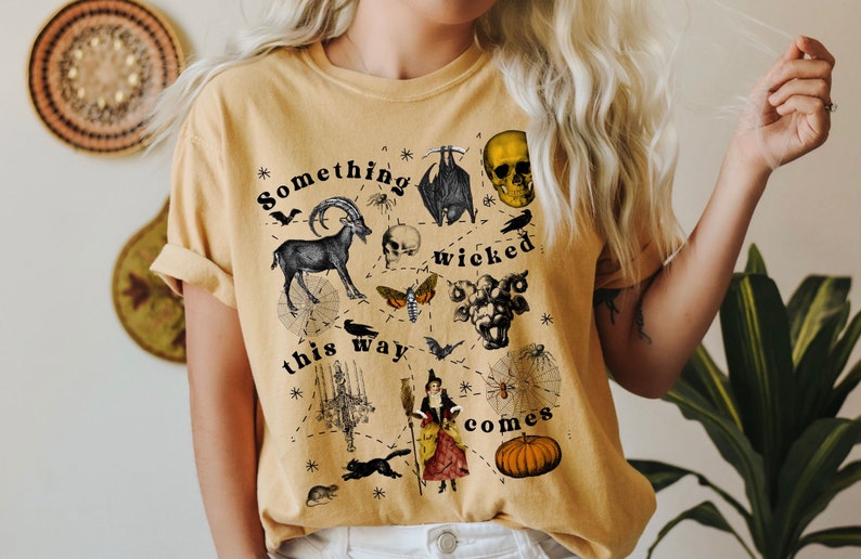 May include: A yellow t-shirt with a black and white graphic print of a skull, a goat, a bat, a moth, a spider web, a witch, a pumpkin, and the text "Something wicked this way comes."