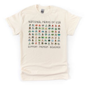 May include: A beige t-shirt with a graphic print of all the National Parks of the USA. The graphic includes the name of each park and a small illustration of a landmark from each park. The text at the bottom of the graphic reads "Support - Protect - Discover."
