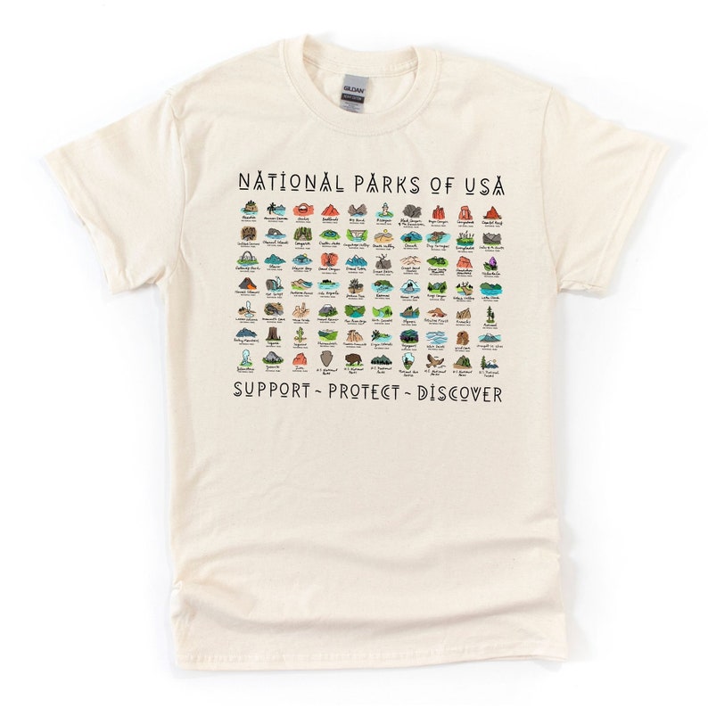 May include: A beige t-shirt with a graphic print of all the National Parks of the USA. The graphic includes the name of each park and a small illustration of a landmark from each park. The text at the bottom of the graphic reads "Support - Protect - Discover."
