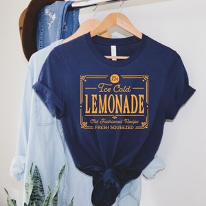 May include: A navy blue t-shirt with a vintage-style graphic design that reads "25&cent; Ice Cold Lemonade. Old Fashioned Recipe. Fresh Squeezed."
