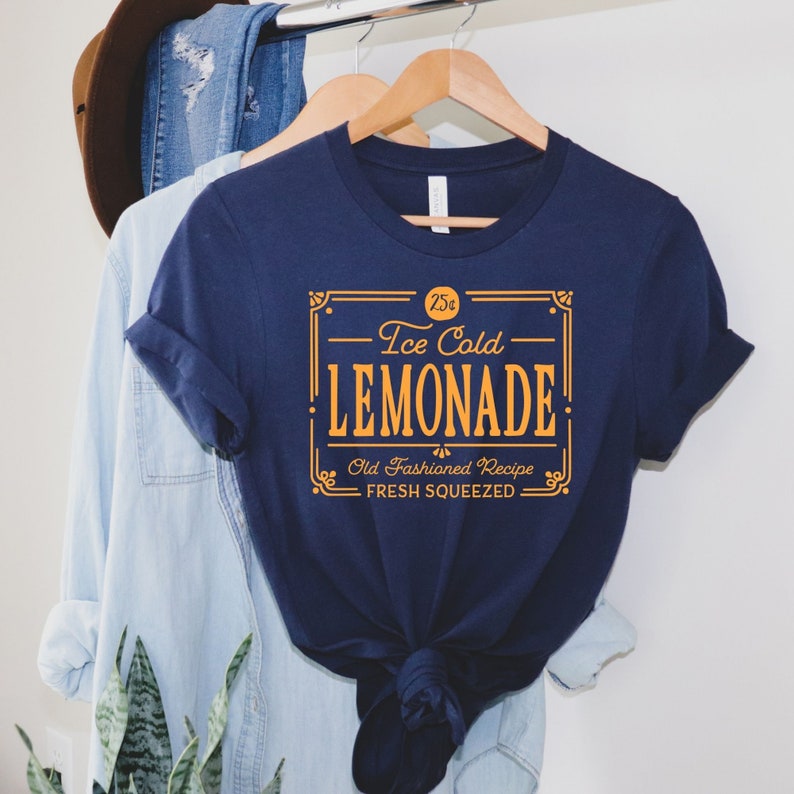 May include: A navy blue t-shirt with a vintage-style graphic design that reads "25&cent; Ice Cold Lemonade. Old Fashioned Recipe. Fresh Squeezed."