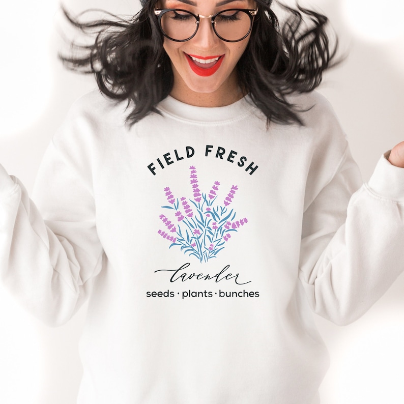 May include: White sweatshirt with a graphic design of lavender flowers and the text "Field Fresh Lavender seeds. plants. bunches"