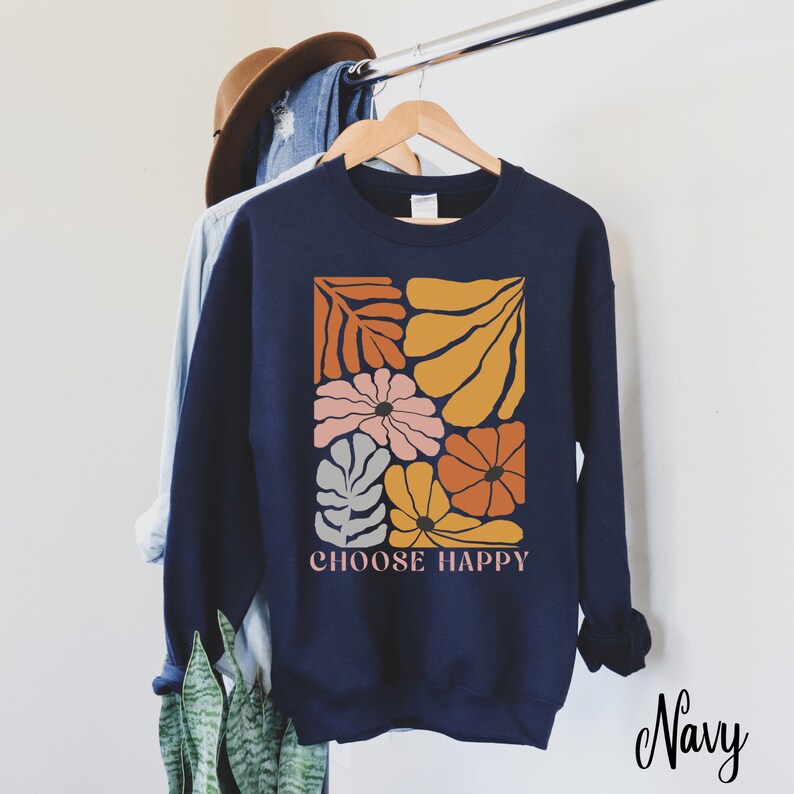 May include: Navy blue sweatshirt with a graphic of colorful flowers and leaves in a square frame. The text "CHOOSE HAPPY" is printed below the graphic.