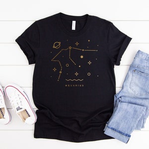 May include: Black t-shirt with a gold outline of the Aquarius constellation and the word "AQUARIUS" printed below.