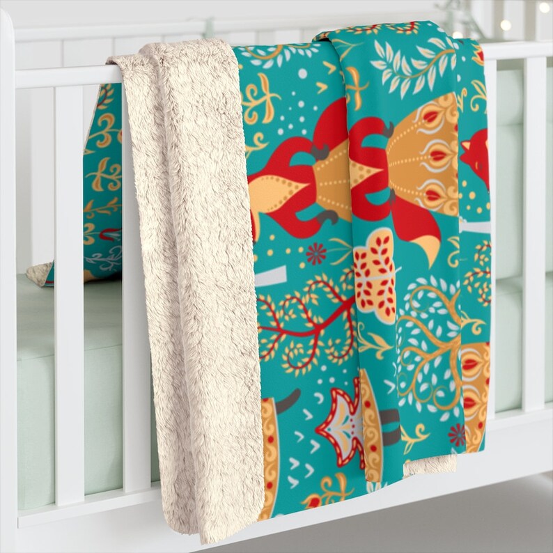 May include: A teal blue fleece throw blanket with a colorful pattern of stylized foxes, trees, and flowers. The blanket has a white sherpa lining.