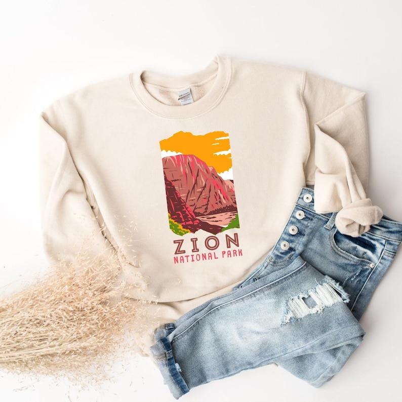 May include: A beige sweatshirt with a graphic design of a mountain range and the text "Zion National Park".