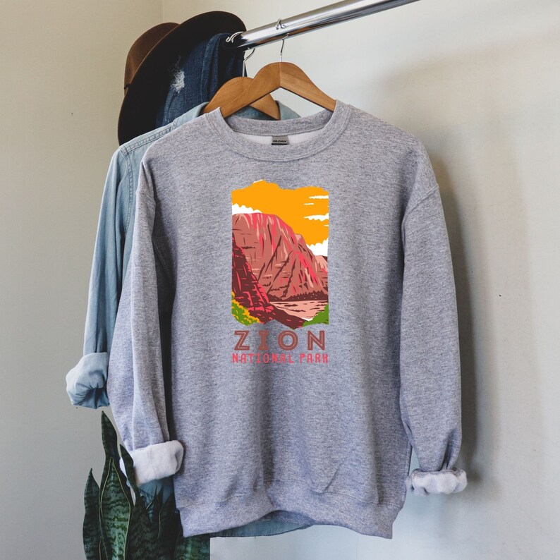 May include: Gray sweatshirt with a graphic of a red mountain range with a yellow sky and the text "Zion National Park".