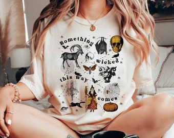 May include: A white t-shirt with a black and white illustration of a skull, a goat, a bat, a spider web, a witch, a pumpkin, and other spooky imagery. The text "Something wicked this way comes" is printed on the shirt.
