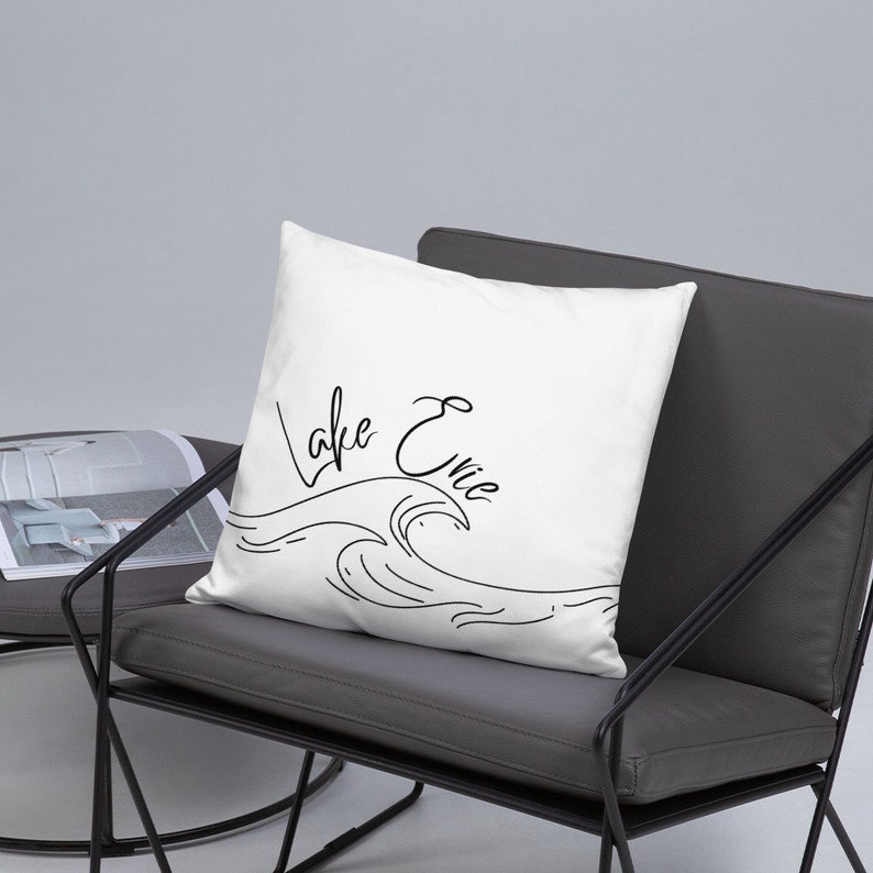 May include: White throw pillow with black cursive text that reads "Lake Erie" and a black line drawing of a wave.