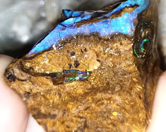May include: A rough, brown, and gold rock with blue, green, and iridescent opal inclusions. The opal is a natural gemstone with a unique and beautiful display of color.