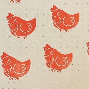May include: A pattern of orange rubber stamps of a stylized chicken on a white background with small black dots.