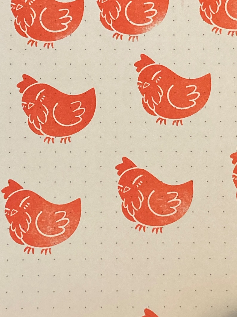 May include: A pattern of orange rubber stamps of a stylized chicken on a white background with small black dots.