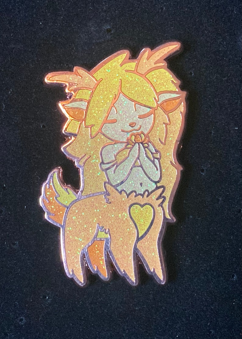 May include: A gold glitter enamel pin of a cartoon fawn with a heart on its back and long blonde hair. The fawn is holding a flower in its hands and has its eyes closed.