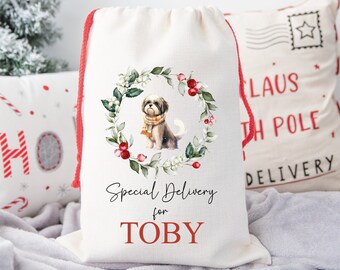 May include: A white canvas Santa sack with a red drawstring. The sack features a watercolor illustration of a dog wearing a scarf in a wreath of greenery with red berries. The text "Special Delivery for TOBY" is printed in red on the sack.  PERSONALISED SANTA SACK is printed at the bottom.