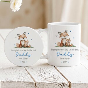 May include: A white ceramic mug and a matching round coaster featuring a watercolor illustration of a fox and a kit. The text reads: Happy Father's Day to the best Daddy love Oliver 2026. The design includes small blue stars and green grass.