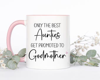 Può includere: Una tazza in ceramica bianca con manico e bordo interno rosa chiaro. La parte anteriore presenta un testo nero che recita: ONLY THE BEST Aunties GET PROMOTED TO Godmother, con una piccola icona a forma di cuore rosa chiaro accanto a Godmother.
