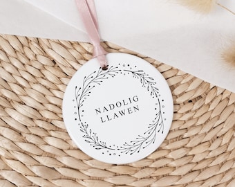 May include: White ceramic ornament with a black floral wreath and the text "Nadolig Llawen" in the center.